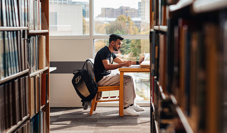Male student sitting at a desk in the library with cityscape in the background. 